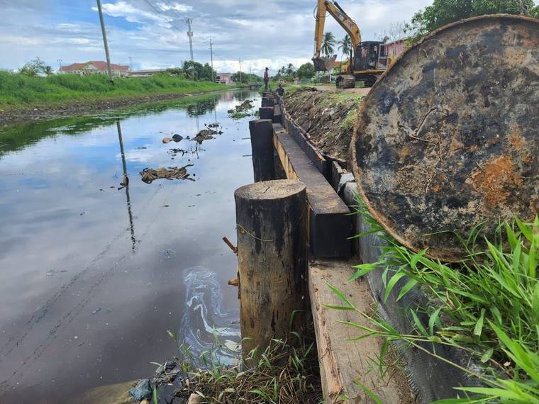 Timber pile revetment along a canal bank with an excavator working