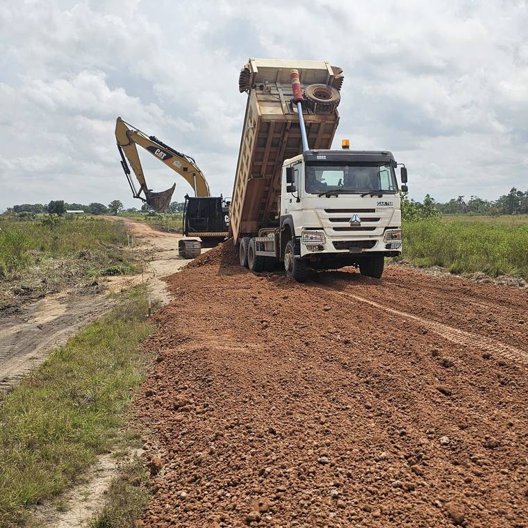 Tipper truck discharging laterite fill beside an excavator